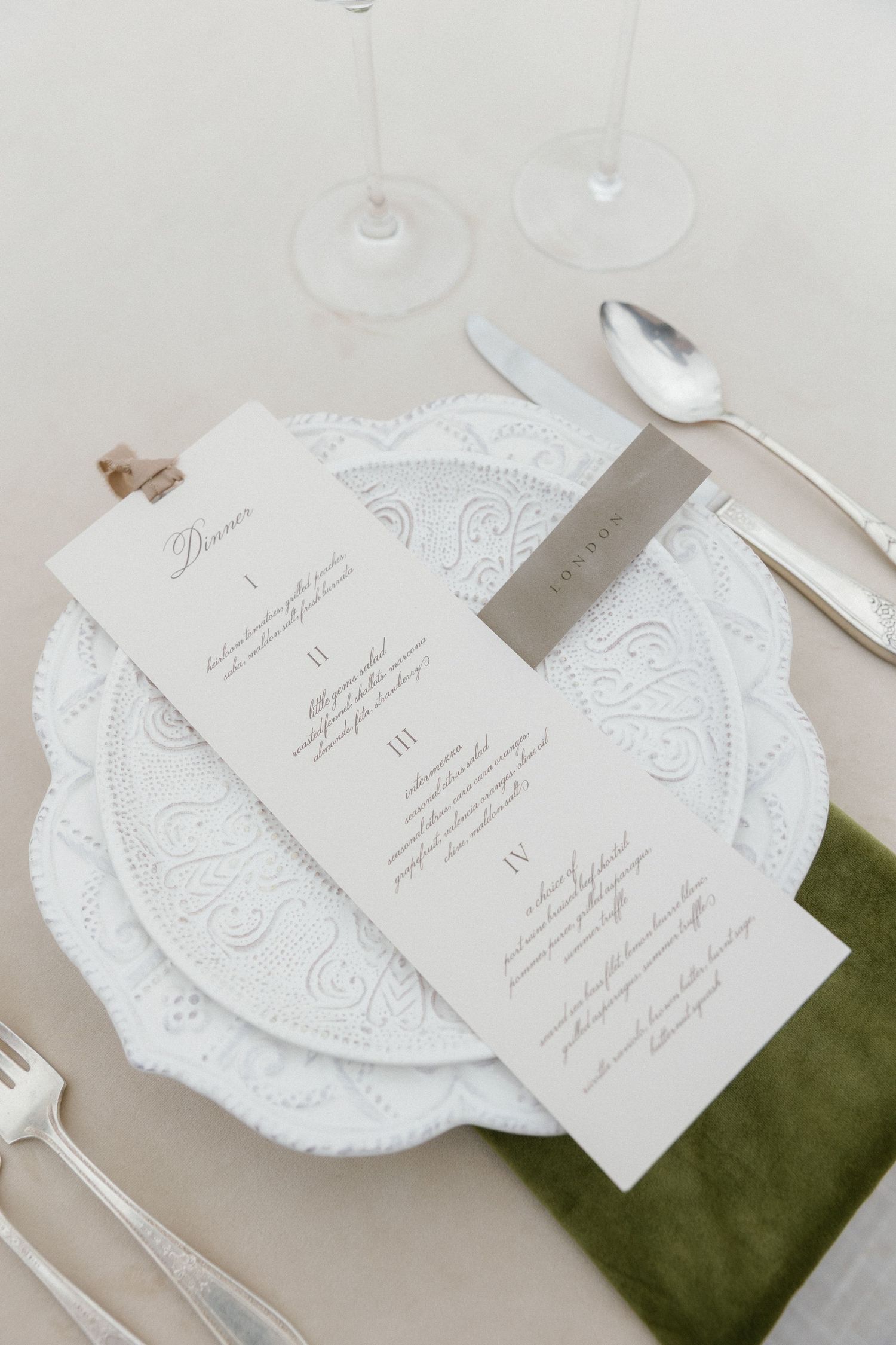 Elegant wedding menu card placed on white lace charger plate with green napkin and dining utensils.