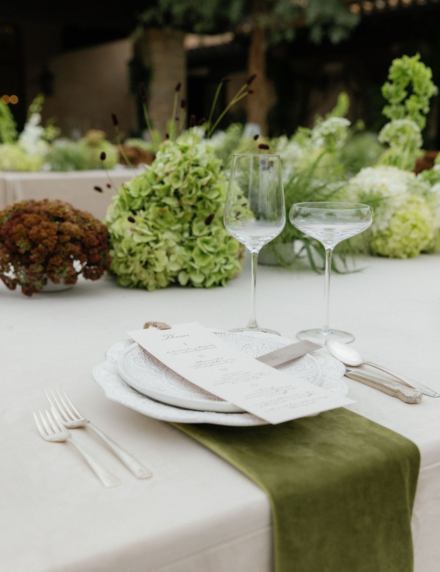 Elegant table setting with white plates, sage green napkin, wine glasses and hydrangea flower arrangements.