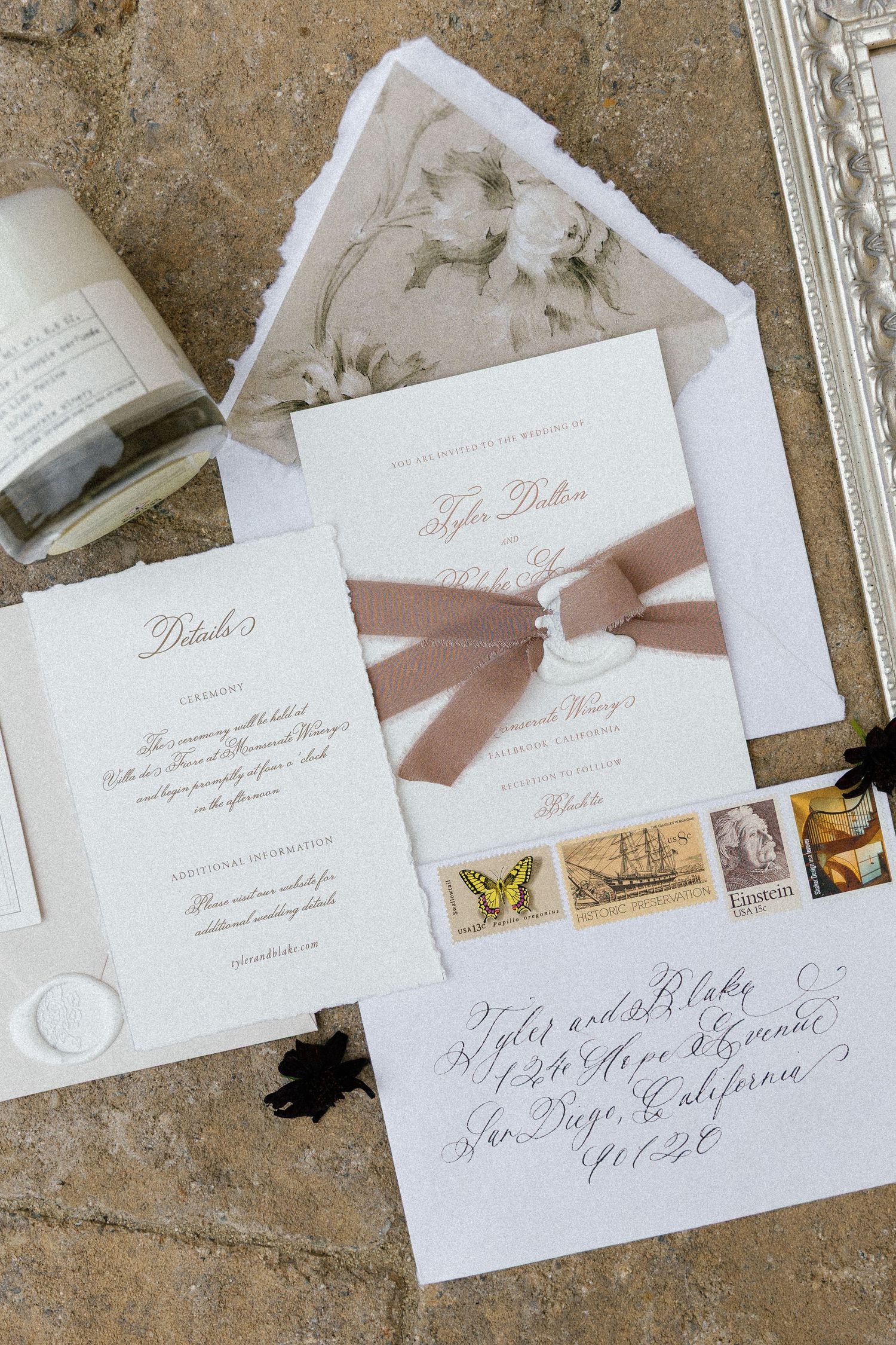 Elegant wedding invitation suite with blush pink ribbon and vintage postage stamps on textured surface.