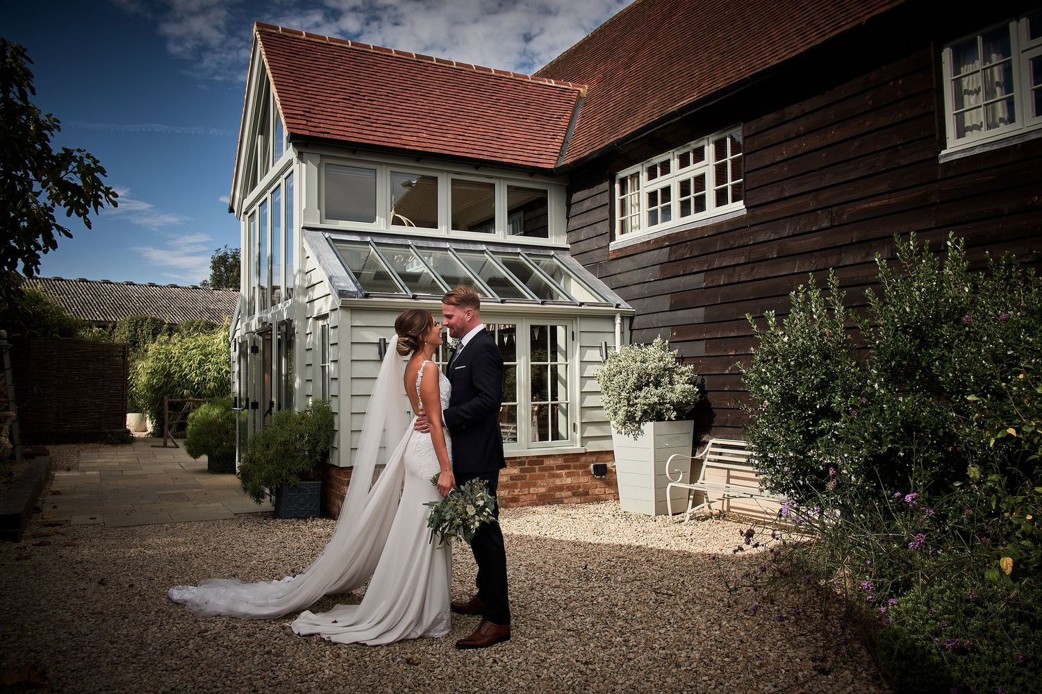 Elegant wedding couple posing against a rustic textured wall with greenery.