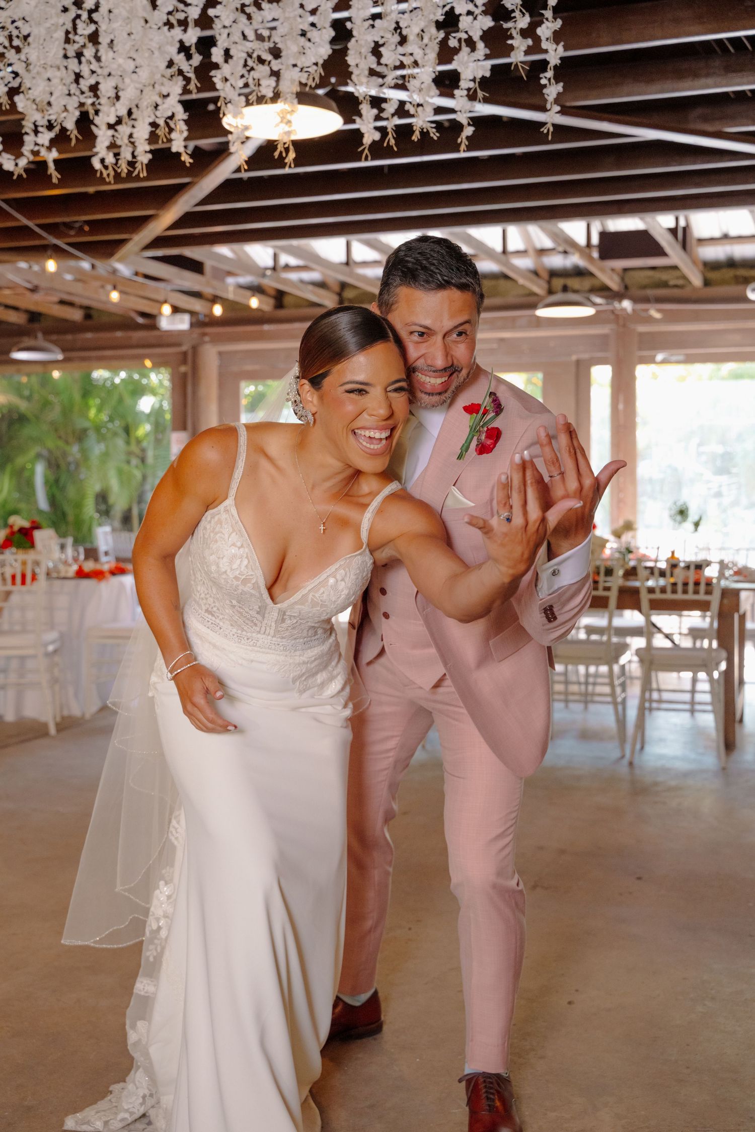 A happy couple shares a candid moment at their wedding reception under crystal chandeliers in an elegant indoor venue.