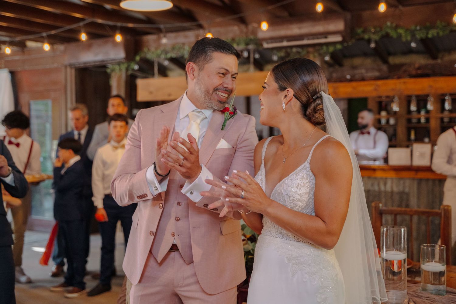 A joyful moment shared during a wedding celebration in a rustic indoor venue with string lights.