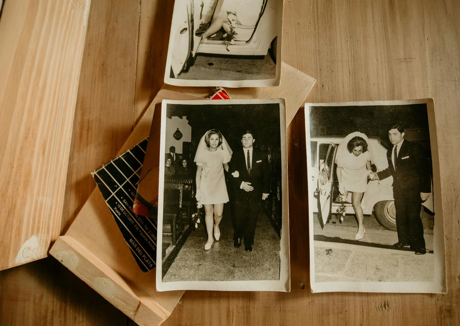 Vintage black and white photographs displayed on wooden surface showing old-fashioned formal occasions and memories.