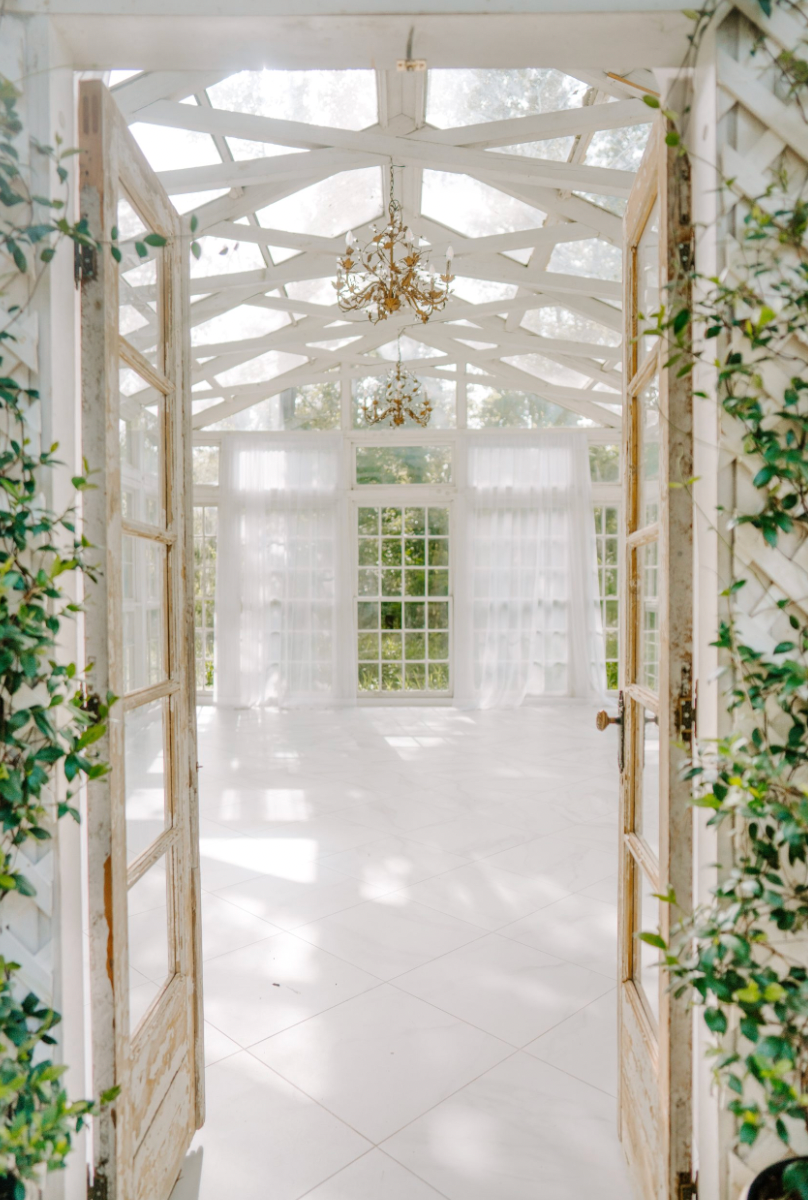 Elegant white greenhouse conservatory interior with climbing vines and antique chandeliers creating a dreamy atmosphere.