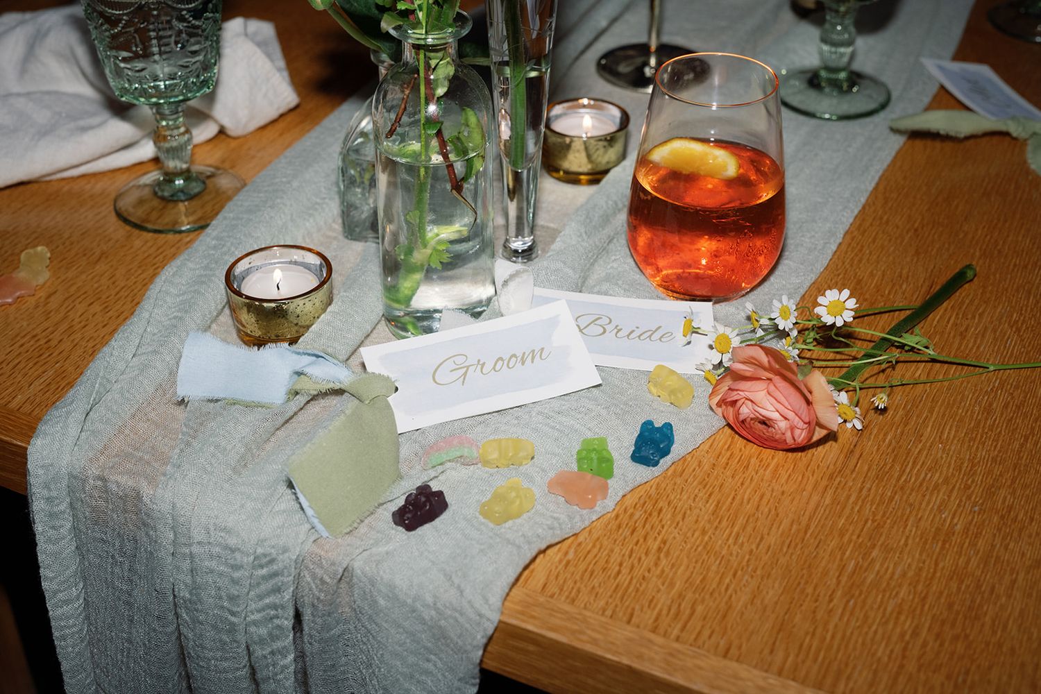 A table setting with scattered crystals, candles, and drinks on a gray linen cloth with decorative elements.