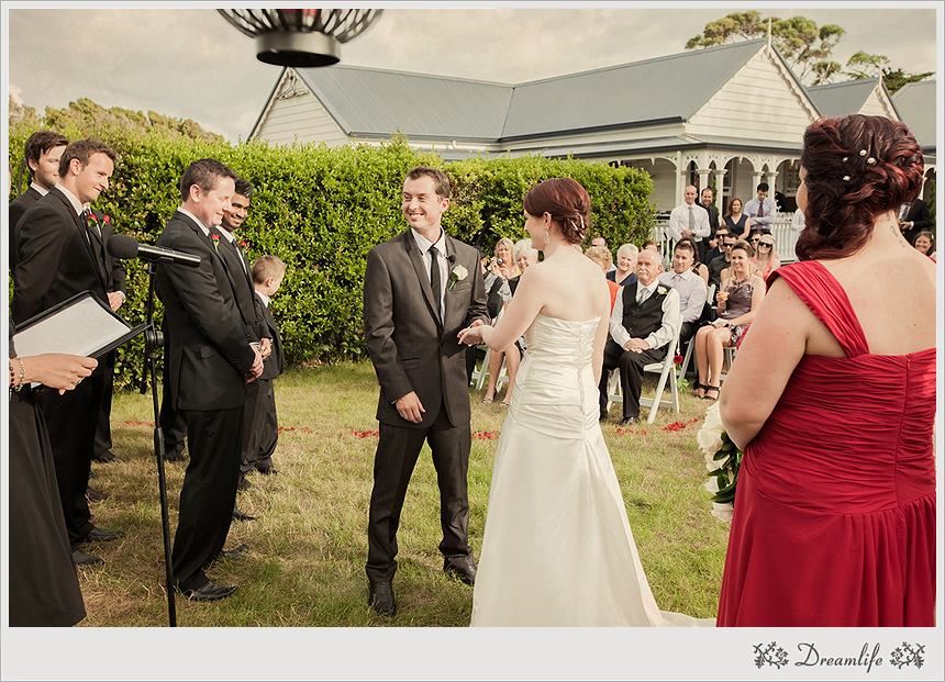 An outdoor garden wedding ceremony with a couple exchanging vows surrounded by guests on a sunny day.