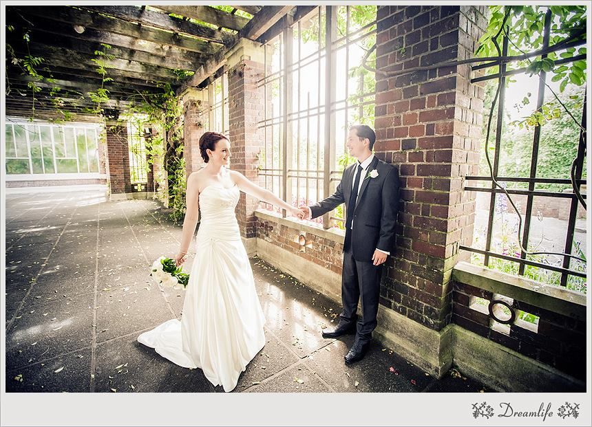 A couple in wedding attire poses for romantic photos in a rustic indoor space with natural light streaming through windows.