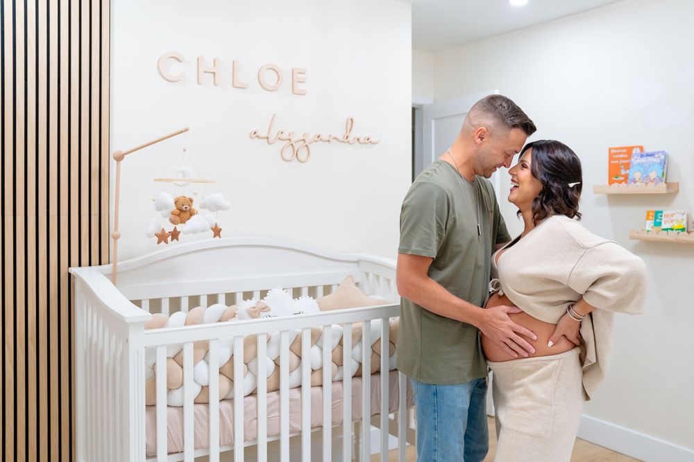 Parents-to-be standing beside a white crib in a serene nursery with modern decor.