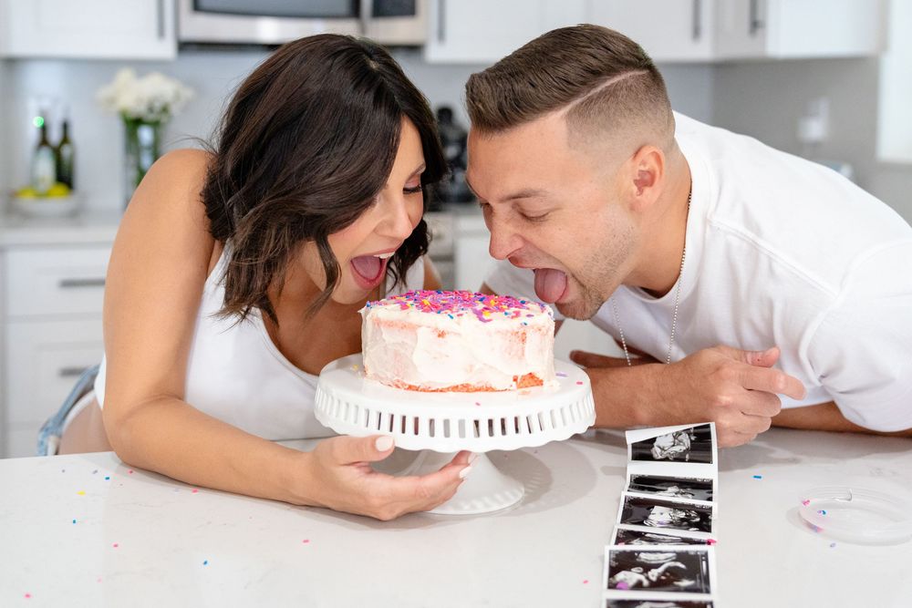 Couple leaning over a white birthday cake with sonogram photos displayed.