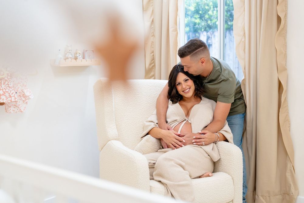 Couple lying together in a white bedroom with natural light streaming through the window.