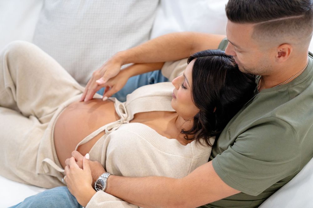 Tender moment between couple as they embrace on couch during maternity photo session.