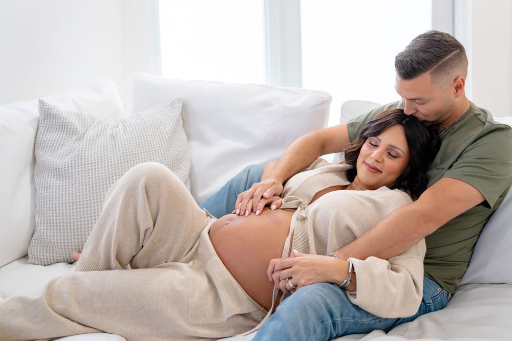 Intimate maternity photo session showing a couple relaxing on a white bed.