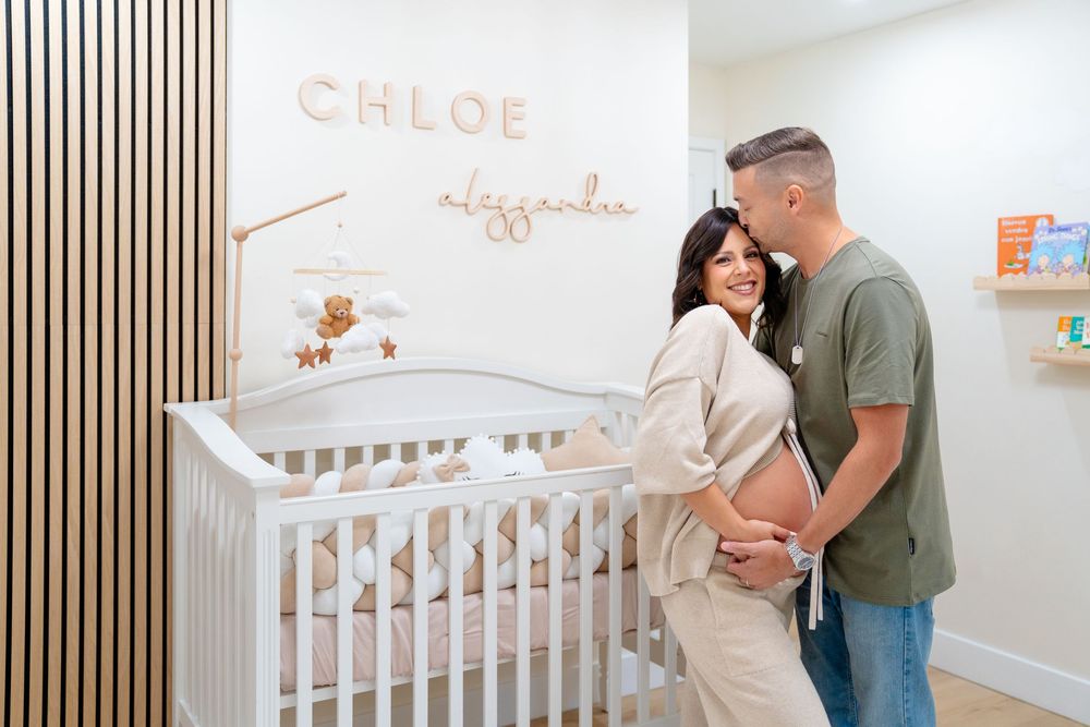 A couple shares an intimate moment in a nursery with a white crib and name decoration on the wall.