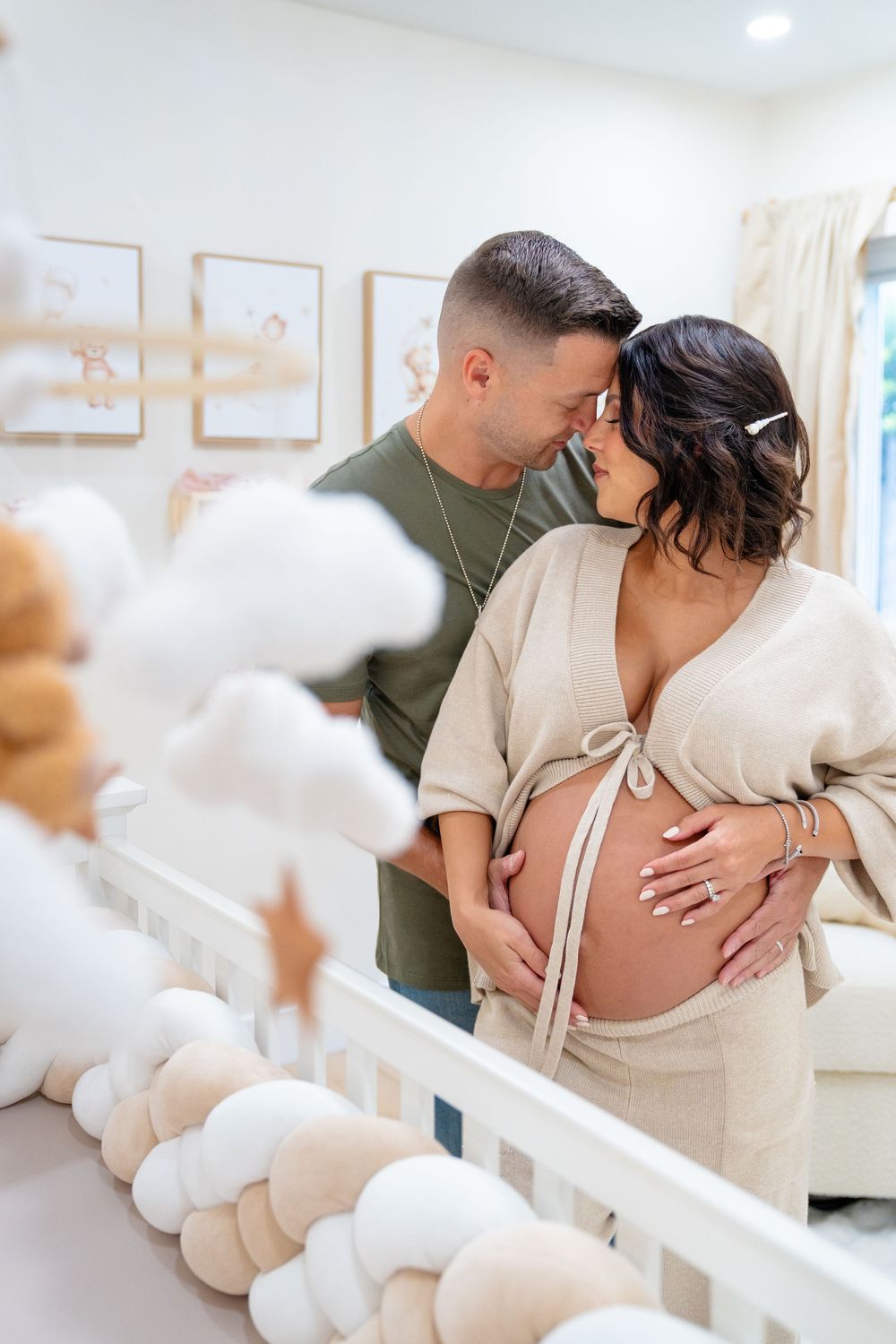 Intimate moment of couple in white and green outfits touching pregnant belly in nursery room.