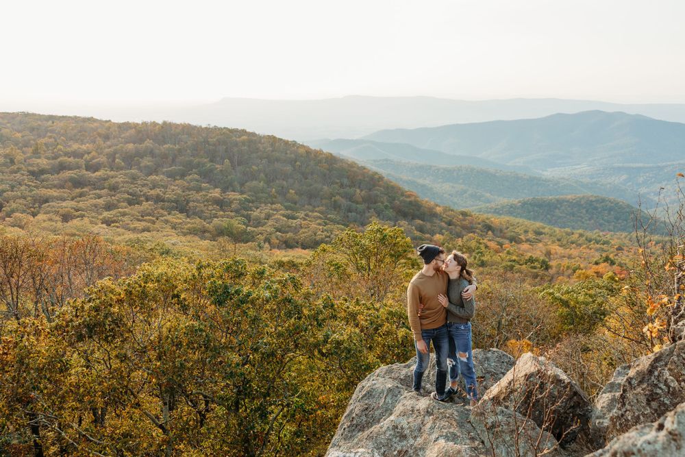 Couple embracing on rocky mountain overlook during autumn season.