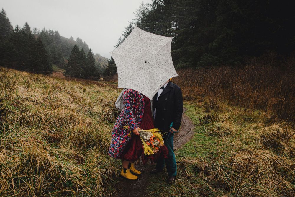 Two people stand close together under a white umbrella on a foggy hillside trail.