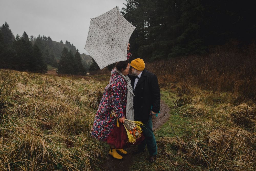 A couple shares an intimate moment under a lace umbrella on a misty mountain slope.