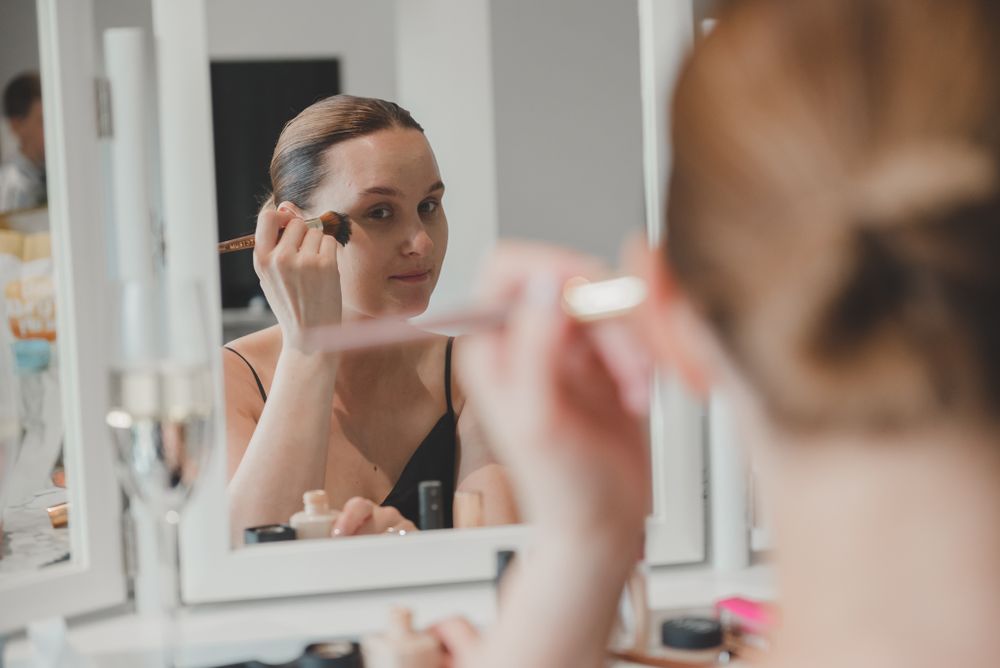 Person applying makeup while looking in vanity mirror.