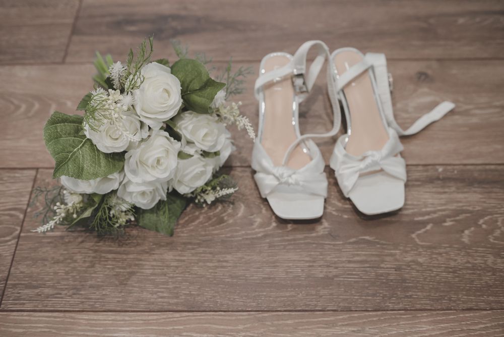 White wedding bouquet and strappy bridal shoes on wooden floor.