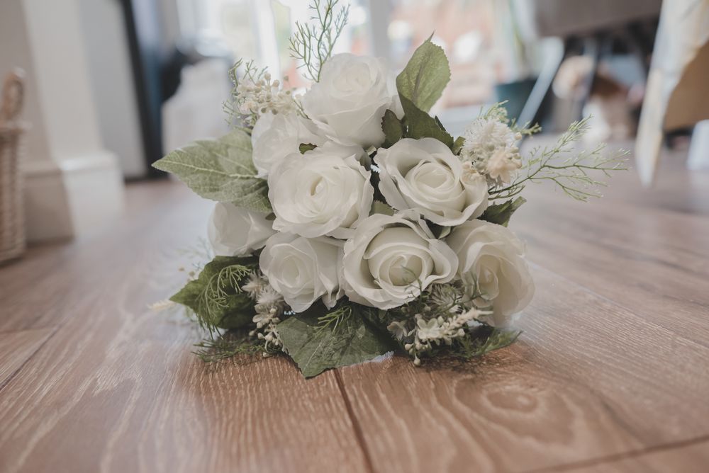 Elegant white rose bridal bouquet with greenery on wooden surface.