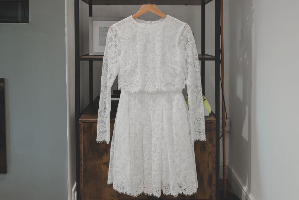 Vintage-style white lace wedding dress hanging on black clothing rack.