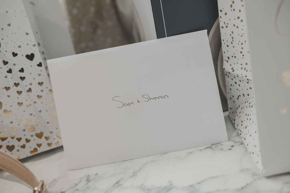 Wedding invitation with names written in silver on white paper with decorative heart details.