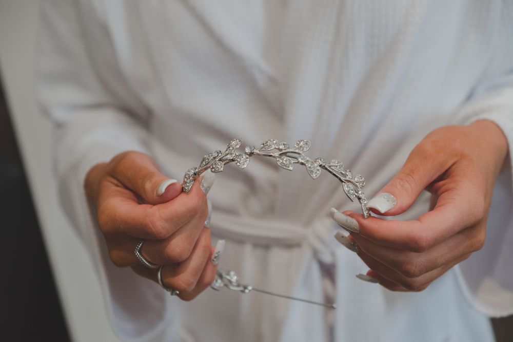 Hands holding delicate silver bridal hair accessory against white fabric background.