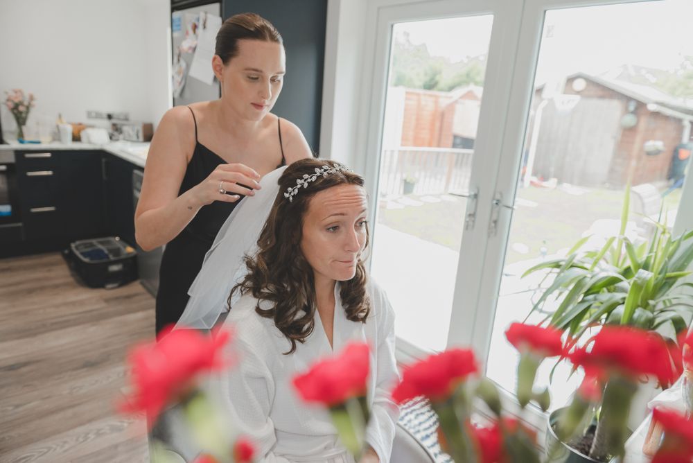 Interior scene of bridal preparation with red flowers and natural window light.