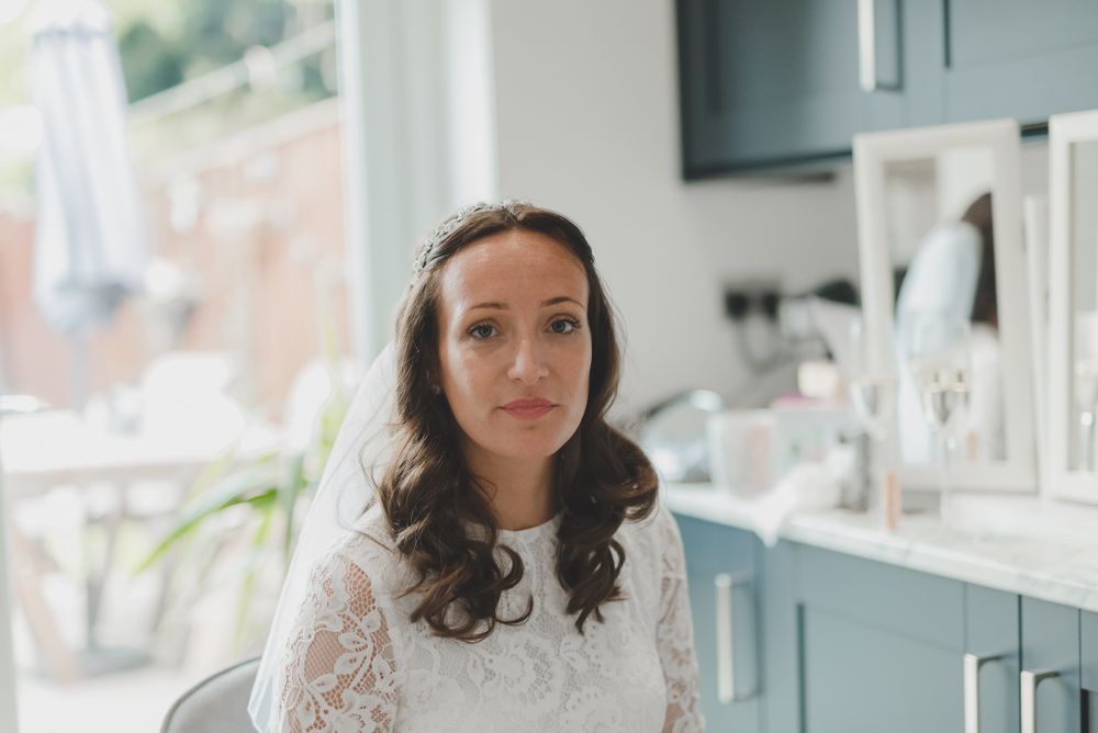 A bride in a white lace wedding dress with long sleeves poses in a kitchen with blue cabinets.