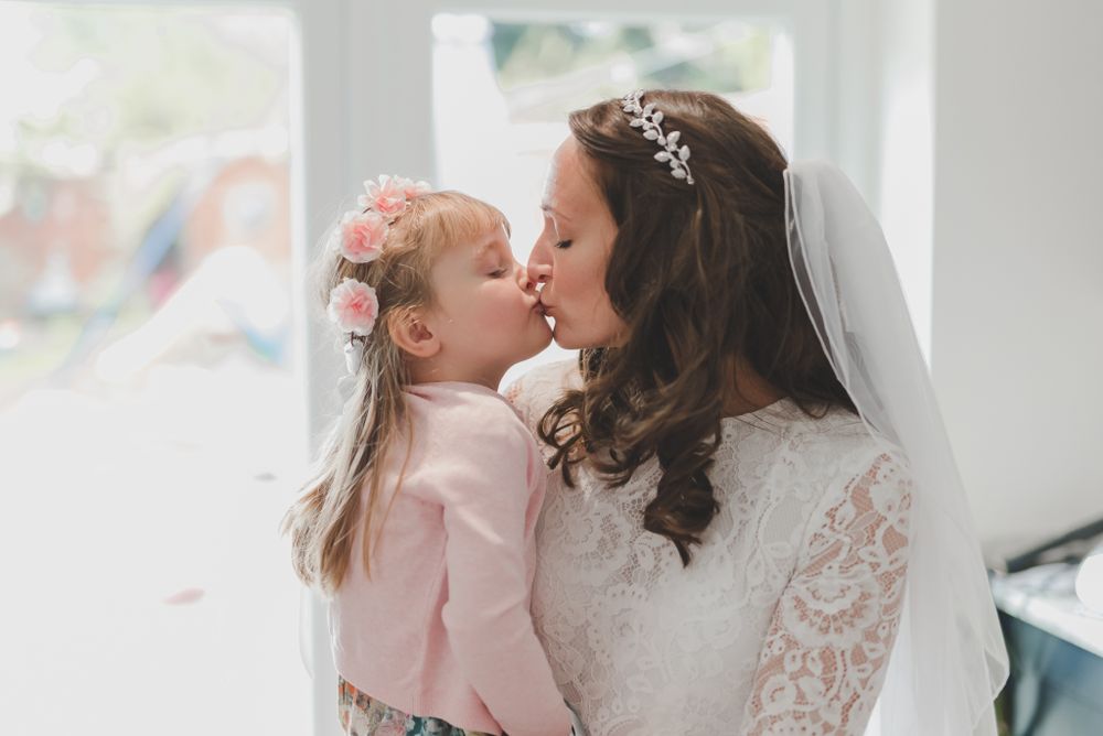 A tender moment between a bride in lace and a small child in pink during wedding preparations.