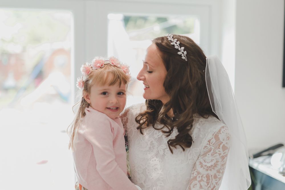 Sweet candid moment between a bride and young child in pink during wedding day preparations.