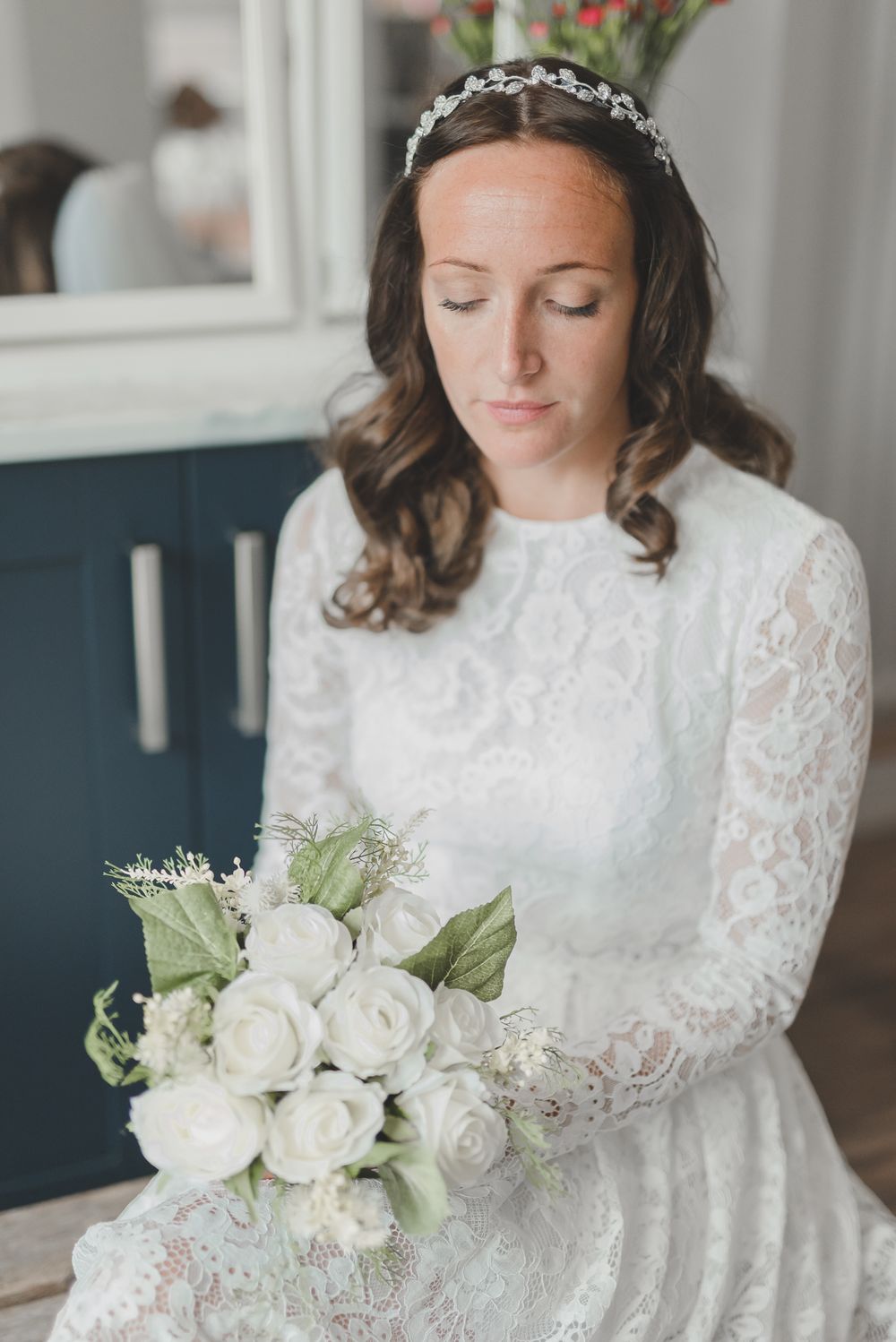 Bridal portrait with white rose bouquet showing intricate lace dress details and delicate tiara.