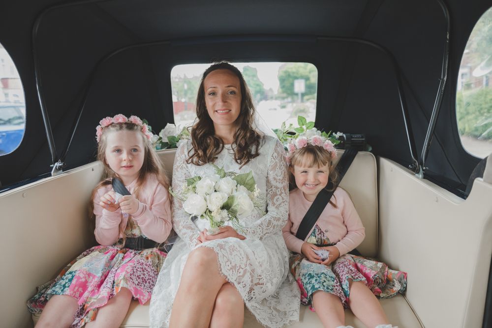 Wedding party sits inside vintage car with bride in center holding white bouquet.