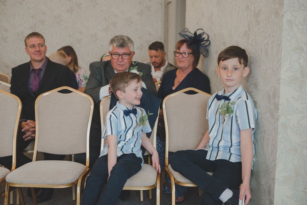 Two young guests in matching blue striped shirts sit on chairs at a formal event.