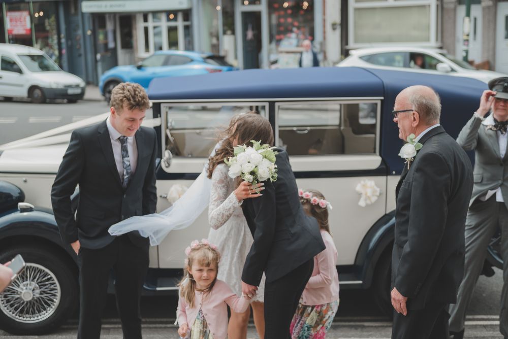 A vintage car adorned for a wedding celebration parked on a city street.