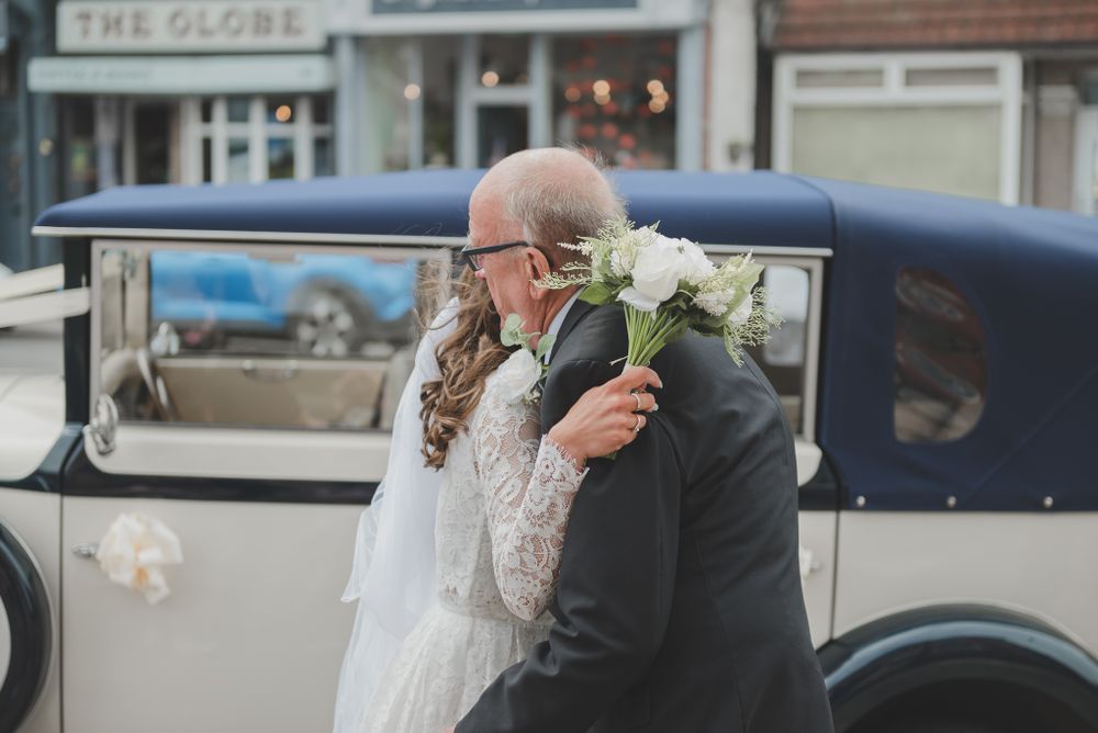 A tender embrace shared during a wedding celebration next to a classic vintage car.