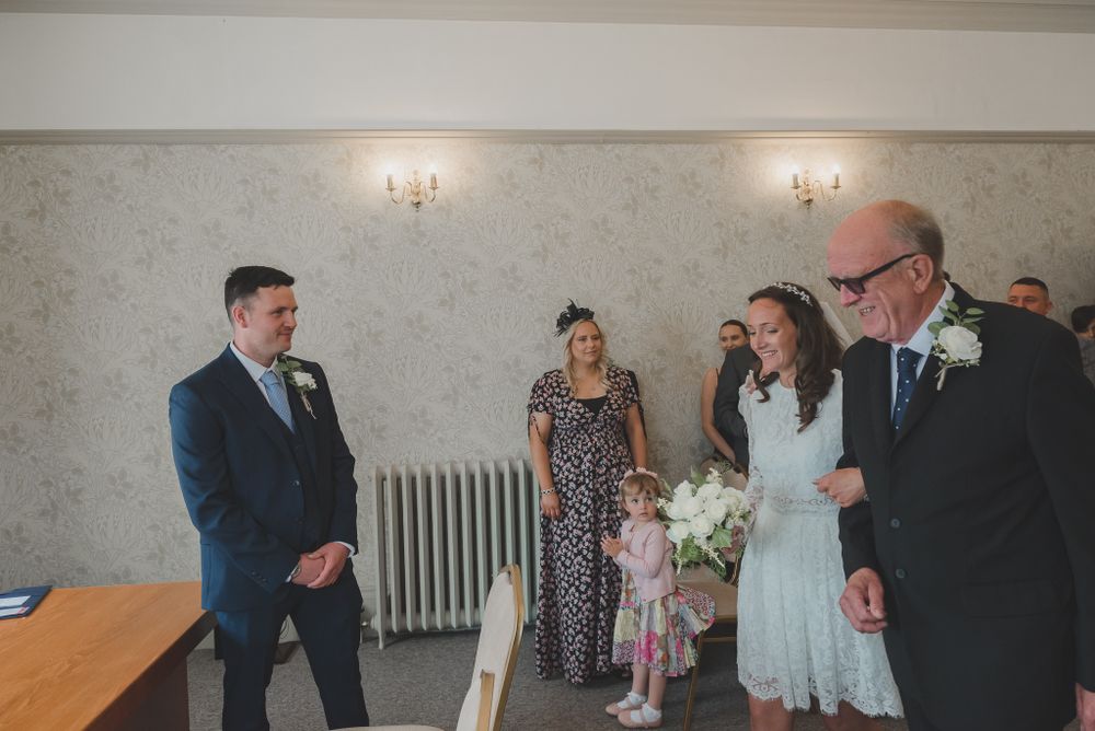 Wedding guests gather in a room with vintage wall sconces and a radiator.