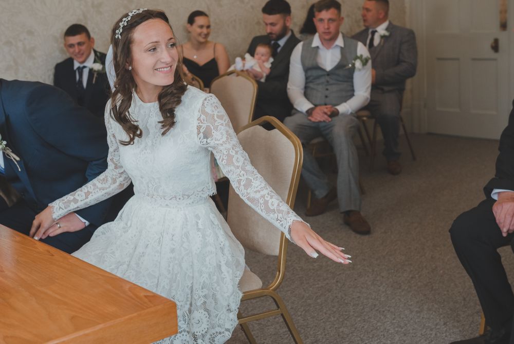 Bride in lace wedding dress gestures expressively during reception celebration.