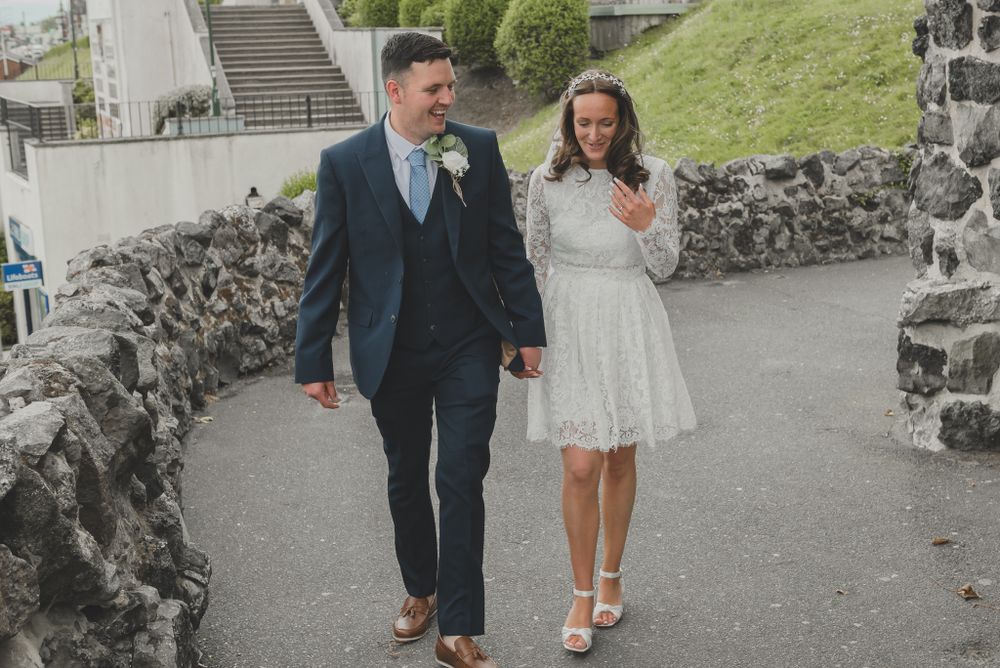 Couple takes romantic stroll along stone wall path in wedding attire.