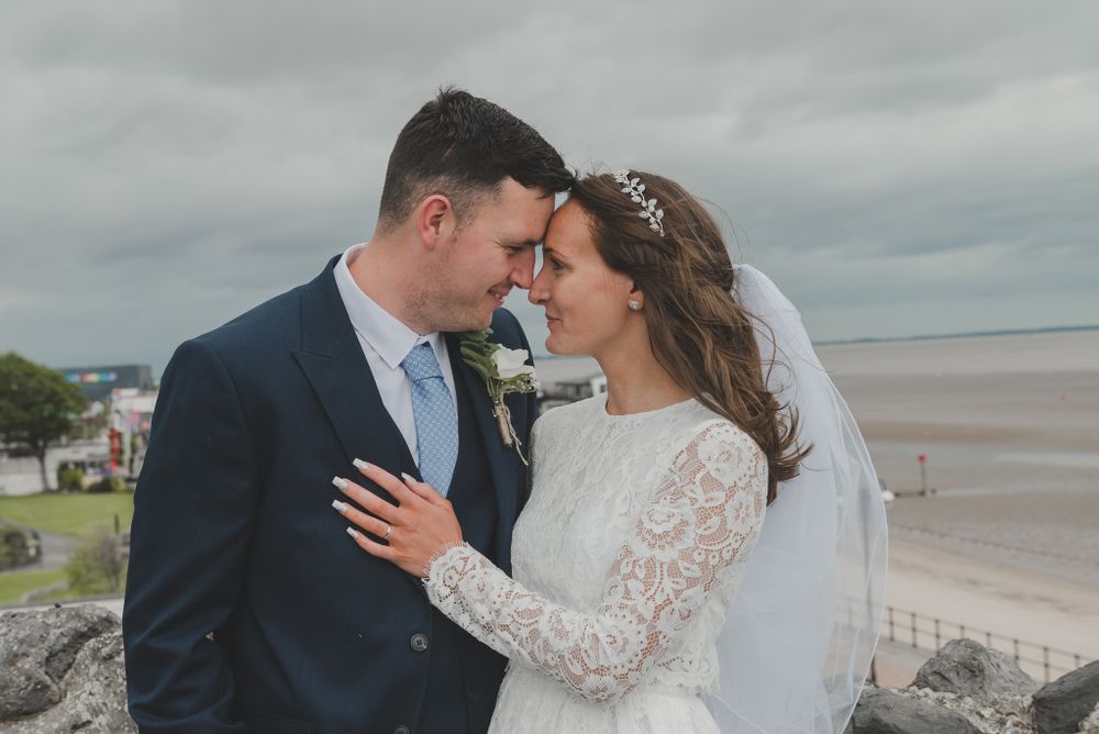 Romantic forehead touch moment captured against moody coastal backdrop.