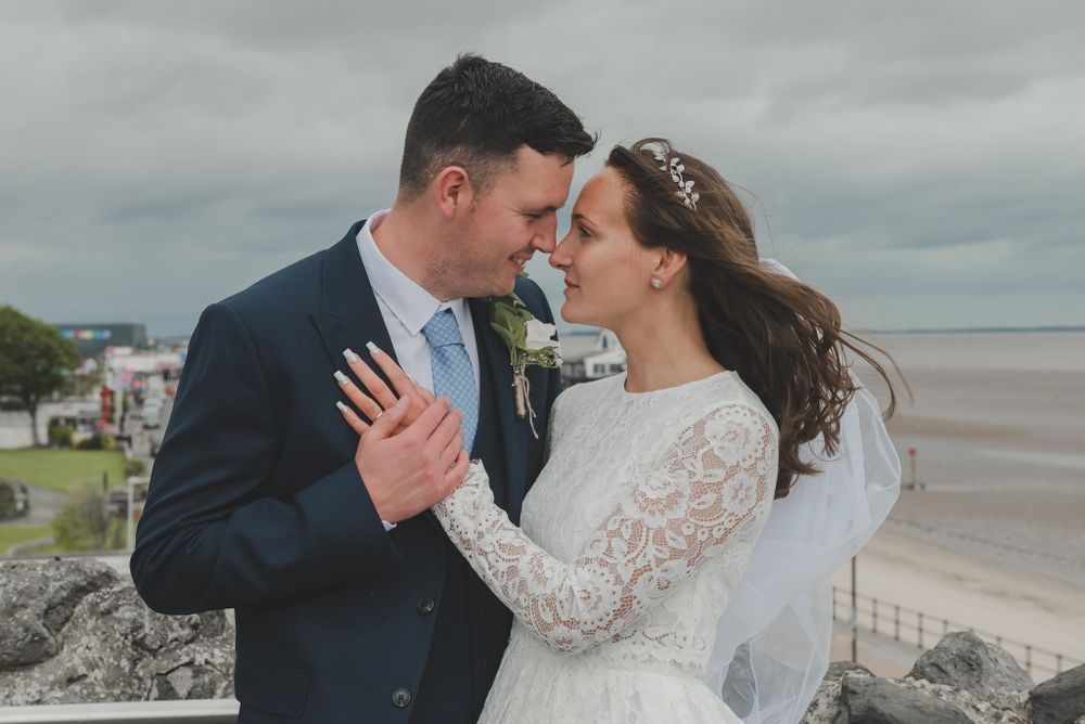 Tender moment shared between newlyweds against dramatic coastal landscape.