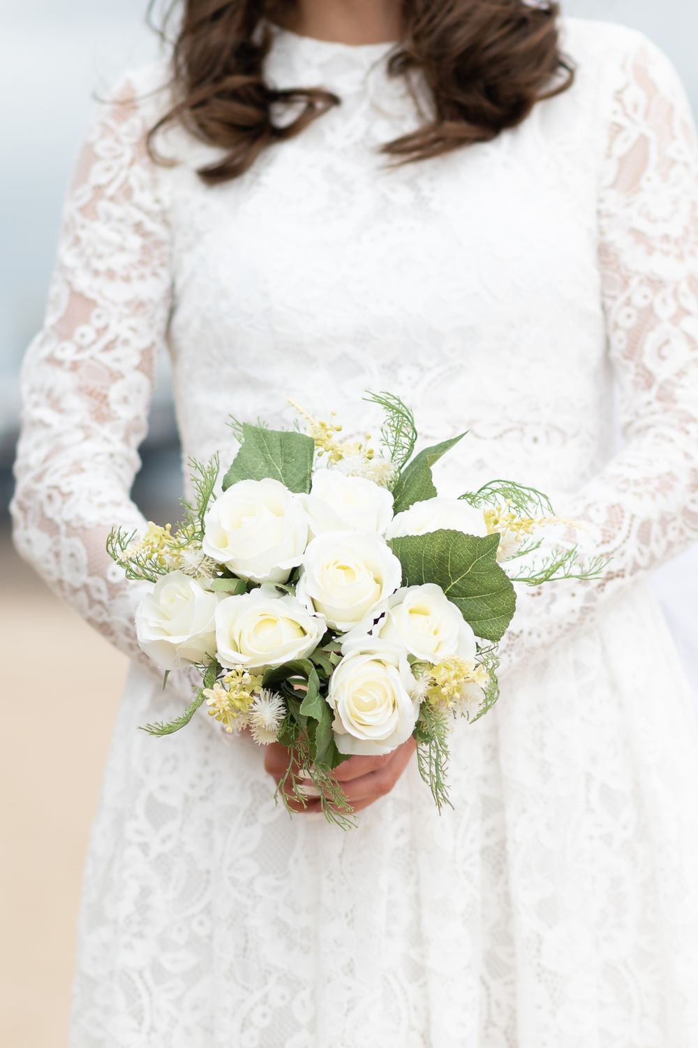 White lace wedding dress detail with bride holding classic white rose bouquet.