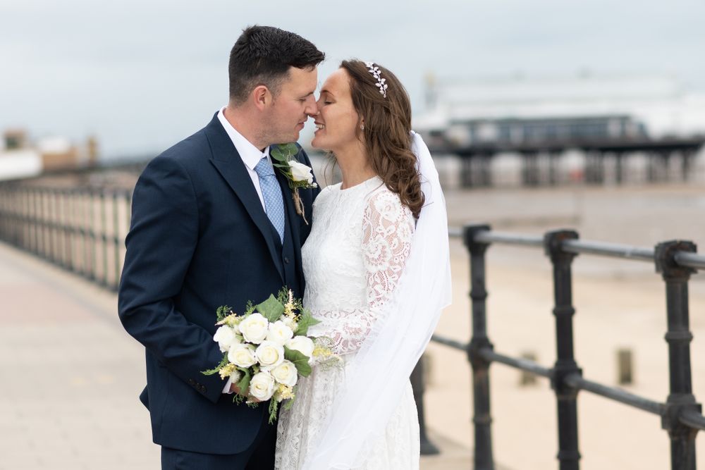 Romantic waterfront moment between newlyweds by iron railings with pier view.