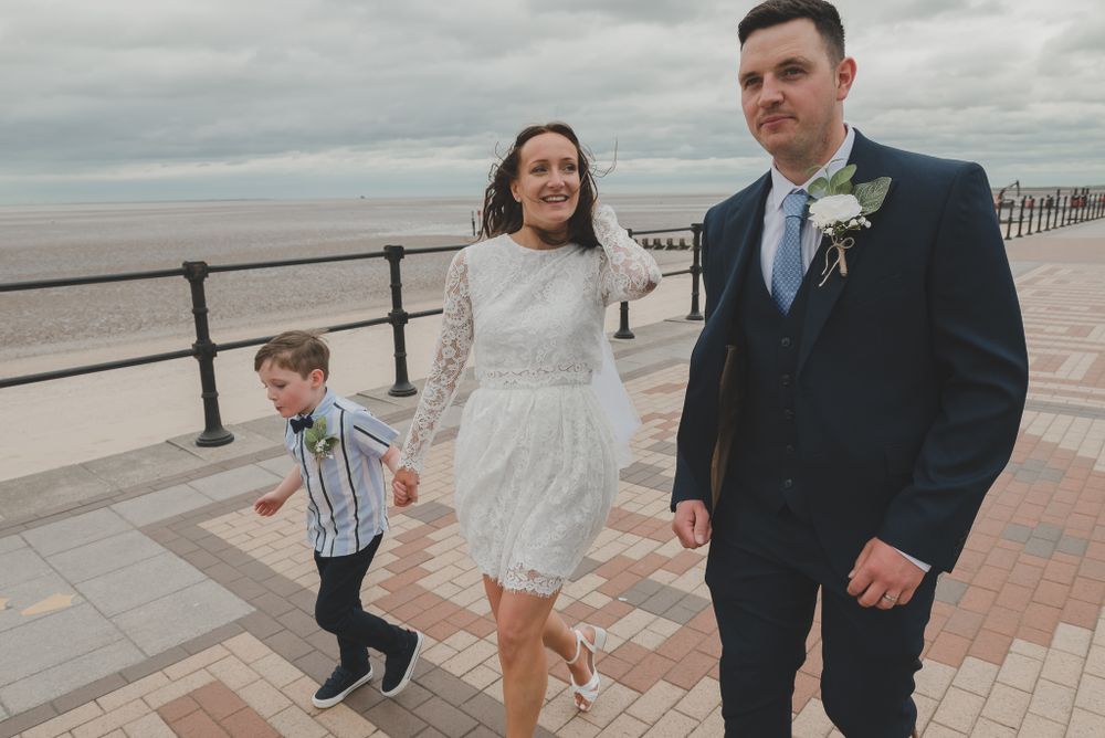 Wedding party walking along seaside promenade on overcast day.