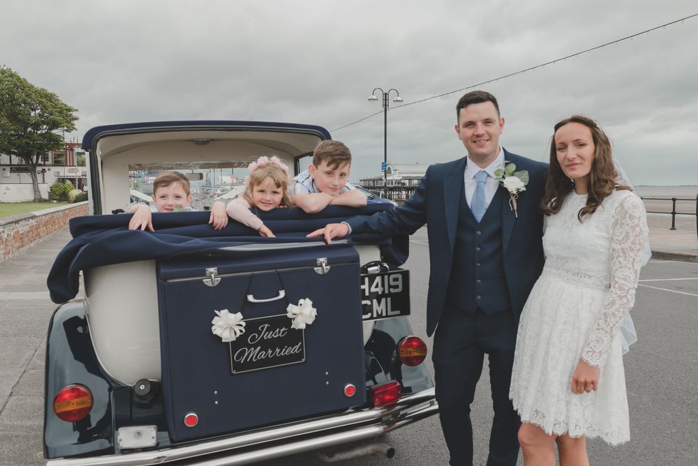 Children peek out from the back of a classic wedding car decorated with flowers.