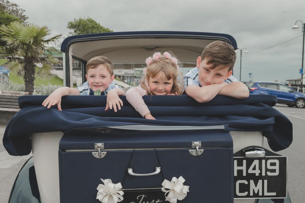Three children playfully pose in the back of a vintage car with license plate H419 CML.