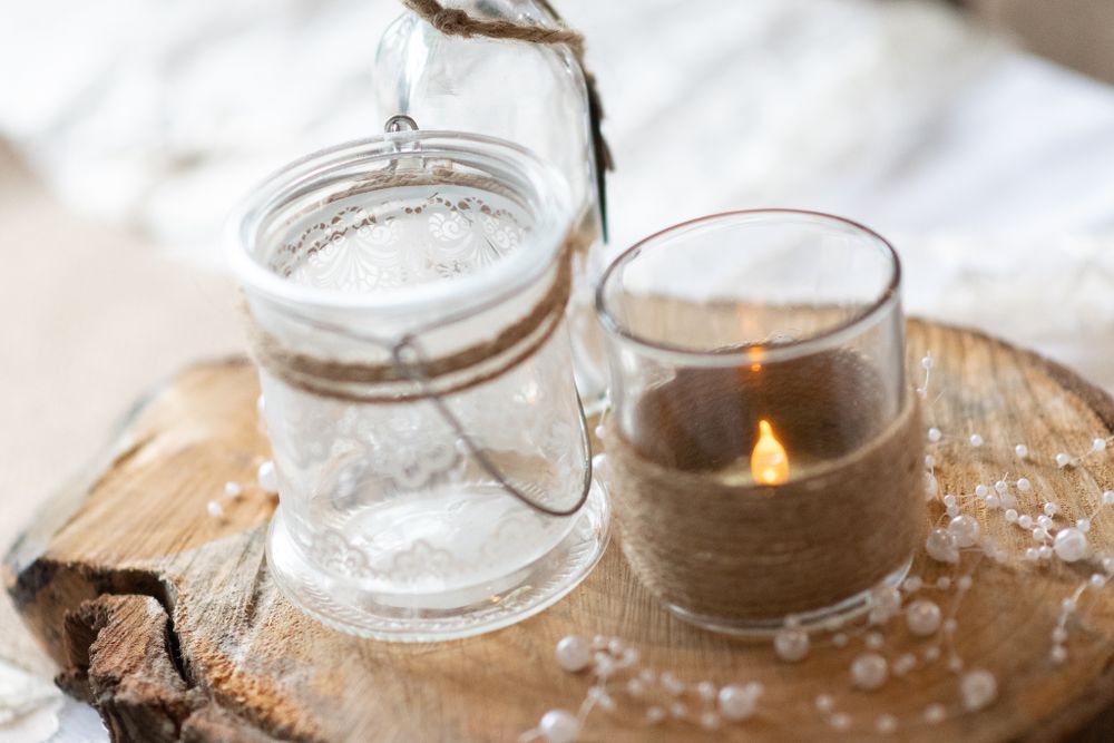 Mason jar candle holders with glowing light sit on rustic wooden surface.