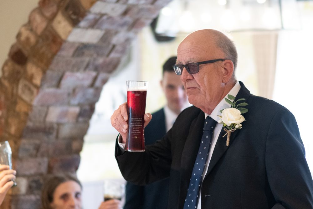 Guest in formal attire raises a glass during reception toast under brick archway.