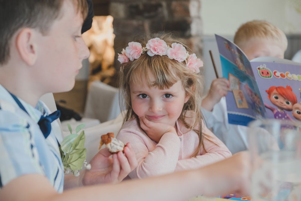 Children in formal wear interact at wedding reception table.