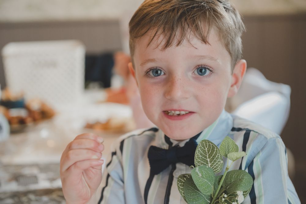 Young attendee in formal attire smiles at wedding reception.